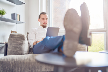 Image of businessman sitting on sofa with tablet in his hands in room.