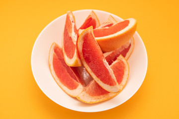 Fresh ripe juicy grapefruit on white plate on yellow background.