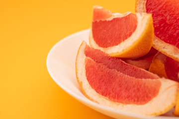 Naklejka na ściany i meble Fresh ripe juicy grapefruit on white plate on yellow background.
