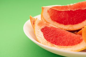 Fototapeta na wymiar Fresh ripe juicy grapefruit on white plate on green background.