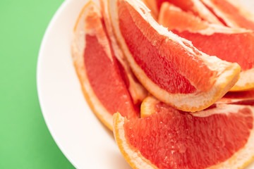 Fresh ripe juicy grapefruit on white plate on green background.