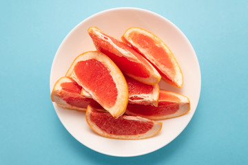 Fresh ripe juicy grapefruit on white plate on blue background.