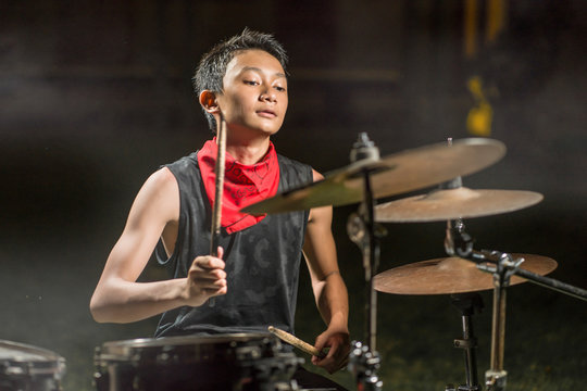 young boy as talented rock band drummer . portrait on stage of handsome and cool Asian American teenager playing drum kit performing night music show