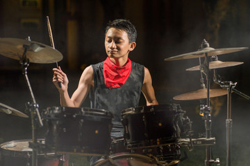  Handsome and cool Asian American teenager playing drum set at home garden emulating night music...