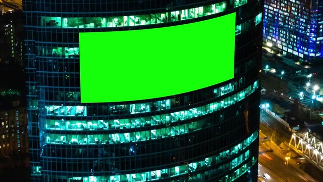 Timelapse: blank green billboard or large display on skyscraper, fast moving cars traffic and warm street light at night. Time lapse, advertising, green screen, mock up, copy space, chroma key concept