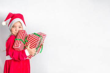 Happy little smiling girl with stack of christmas gift boxes. background caucasian blonde girl in santa red dress, white background copy space. Christmas greeting card concept.