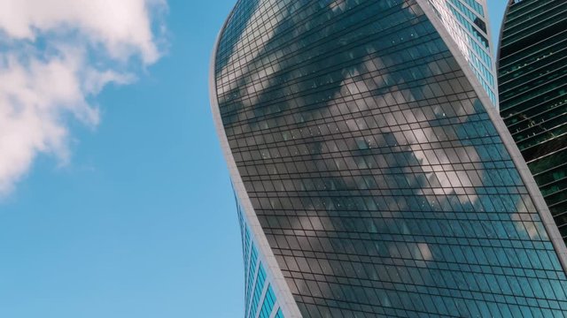 Timelapse - reflection of moving white clouds and blue sky in glass wall of modern tall building, skyscraper - low angle view. Architecture, corporate, business, urban, time lapse, cityscape concept