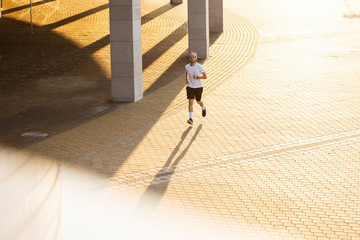 Attractive fit man running in the city at sunset. Fitness, workout, sport, lifestyle concept