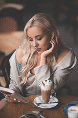 Beautiful blonde girl reading paper book in cafe drinking coffee close up. Breakfast time. Good morning.