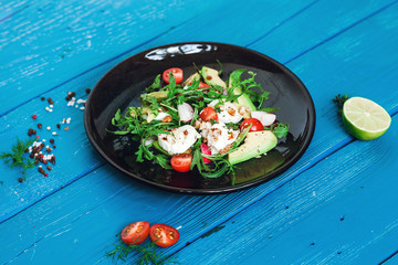 salad of arugula, avocado, cottage cheese, radish and cherry tomatoes on a black glossy plate