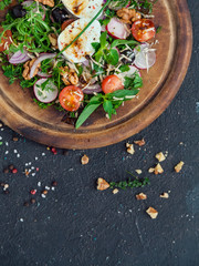 salad on a round wooden cutting board. Ingredients: soft-boiled egg, radish, cherry tomatoes, greens, red onions, arugula, dill, parsley, mint, walnuts, spices, cheese