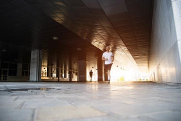Attractive fit man running in the city at sunset. Fitness, workout, sport, lifestyle concept