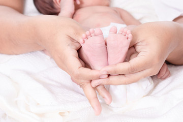 Selective focus mother hands hold her tiny bare feet newborn daughter with carefully