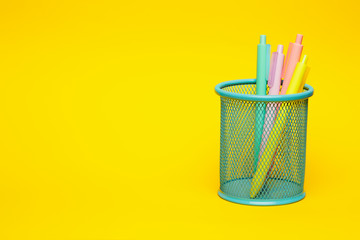 Blue pencil basket holder with colored pens on vivid yellow background with negative space. - 293145246