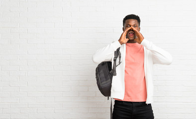 Young afro american man student shouting with mouth wide open and announcing something