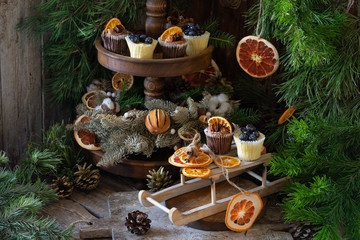 Christmas cupcakes made of white and dark chocolate, decorated with berries, nuts and slices of tangerines. Christmas decor in Scandinavian style. A wonderful composition for a Christmas card