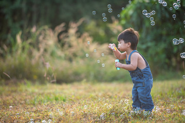 Little boy blowing soap bubbles outdoor at sunset - happy carefree childhood