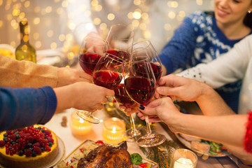 holidays and celebration concept - close up of happy friends having christmas dinner at home, drinking red wine and clinking glasses