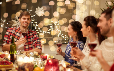 holidays and celebration concept - happy friends with glasses of wine having christmas dinner and speaking toast at home
