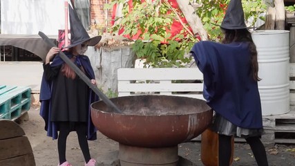 Two little girls in witch costumes brew a magic drink in an abandoned old building. Halloween concept. Slow motion