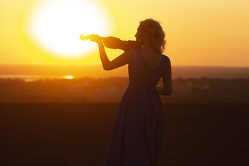 silhouette of a female figure in a long dress playing the violin on a natural background, woman...