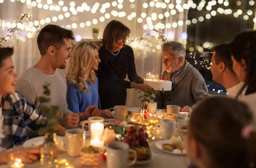 celebration and family concept - happy grandfather blowing candles on birthday cake at dinner party...