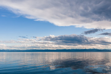 white clouds over the wavy surface of a blue lake. mountains on the other side of Lake Baikal