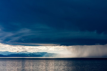 Storm with heavy rain and bright sun over the shore of lake Baikal