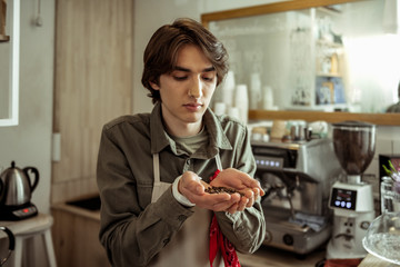 Handsome dark-haired barista enjoying scent of coffee beans