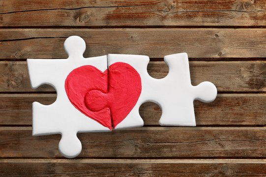 Puzzle pieces with a painted red heart on wooden background