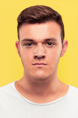Obraz premium Caucasian young man's close up portrait on yellow studio background. Beautiful male model with well-kept skin. Concept of human emotions, facial expression, sales, ad. Looks serious and calm.