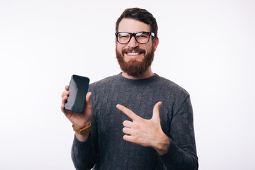 Man pointing at his blank screen phone. He is wearing glasses and a gray sweater.
