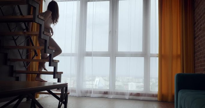 Young woman opens curtains and dancing near big panoramic window.