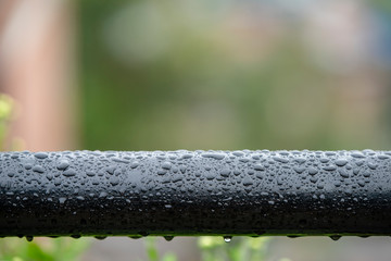 Black pipe covered with raindrops on a greenery background