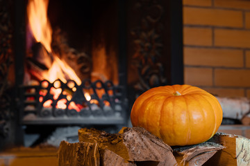 Halloween pumpkin lies on birch wood in front of a blazing fireplace. Mystical holiday Halloween.