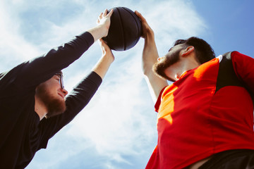 Fototapeta premium Two young bearded athlete guys are playing basketball. One performs the block. Defense and attack during a basketball game. The fight for the right to control the ball. Competitions and confrontation.