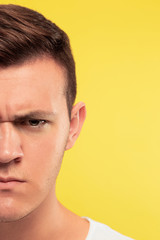 Fototapeta premium Caucasian young man's close up portrait on yellow studio background. Beautiful male model with well-kept skin. Concept of human emotions, facial expression, sales, ad. Looks angry, serious.