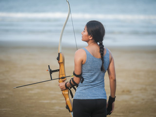 Asian Archery woman with bow shooting on the beach