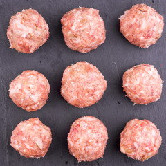 Nine raw meatballs on a dark slate background close-up