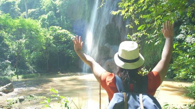 Back view of Backpacker Asian woman walking in forest and relaxing enjoying open arms at waterfall. Hikers hiking in forest travel adventure Asia Thailand