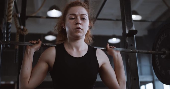 Young beautiful red haired athletic woman straining hard lifting heavy barbell in large professional gym slow motion.