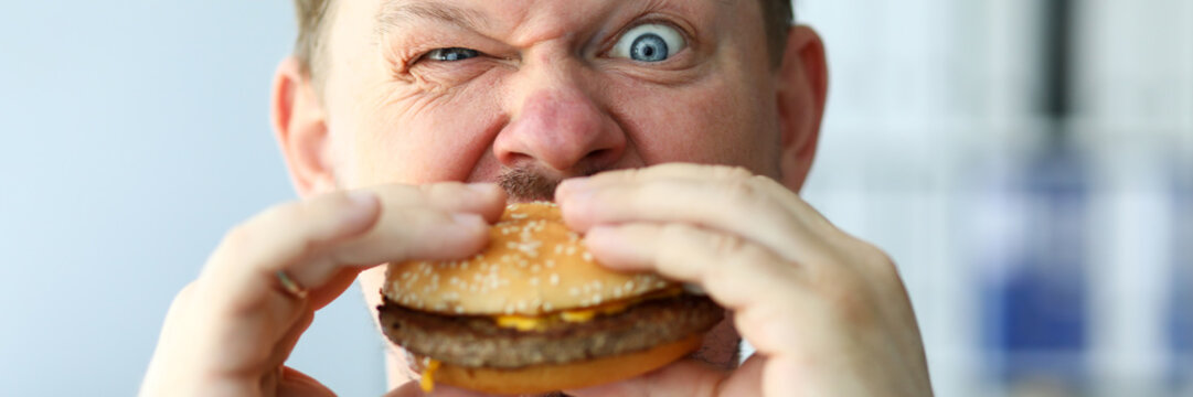 Funny Bearded Man With Idiot Facial Expression Eating Big Burger With Enjoyment Portrait