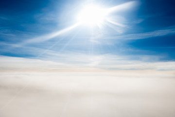 Cloudscape view with horizon line, bright sun and airplane wing