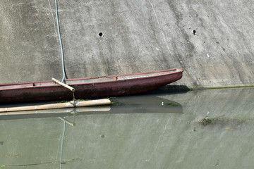 Rustic tiny boat anchored at the polluted river bank