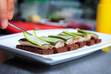 Cook prepares appitizers in the restaurant kitchen. Tasty appetizer with black caviar and cucumber on plate.