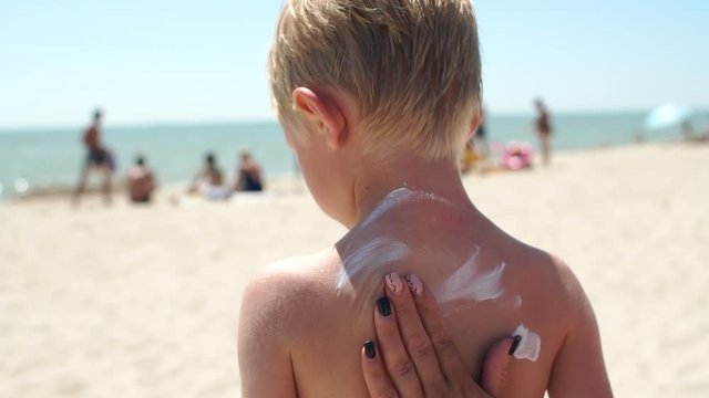 Close-up of a woman's hand applying sunscreen to her young child's skin before tanning in the bright sun by the sea. Protection of the skin from ultraviolet sunlight. Sun protection.
