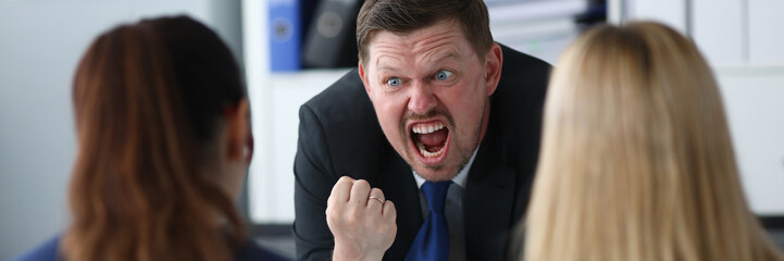 Portrait of screaming businessman angrily looking at guilty business worker made important mistake. Serious male standing in big modern corporate cabinet. Blurred background
