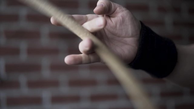 Close up of man hand with black fabric bracelet on his wrist holding drumstick and rotating it with the help of his fingers on a red brick wall background. Action. Musical instruments concept.