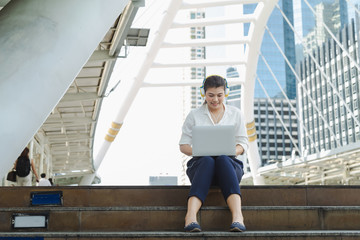 An Asian woman sitting on floor and listening music from headphone.