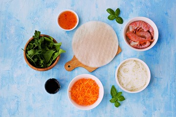 Ingredients for cooking spring rolls: sheets of rice paper, rice noodles, grated carrots, shrimps, salad mixture, soy sauce, chili sauce, basil. Top view. Vietnamese cuisine.